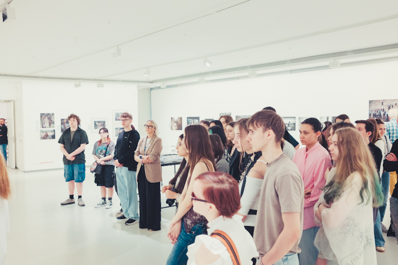 Schülergruppe in der Ausstellung mit Blick auf verschiedene Fotopräsentationen an der Wand