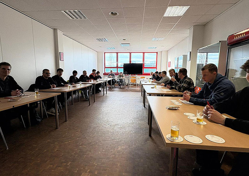 SChüler/-innen sitzen an Tischen in einem langen Raum