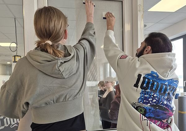 Ein Fensterscheibe wird von zwei Personen mit Folie beklebt