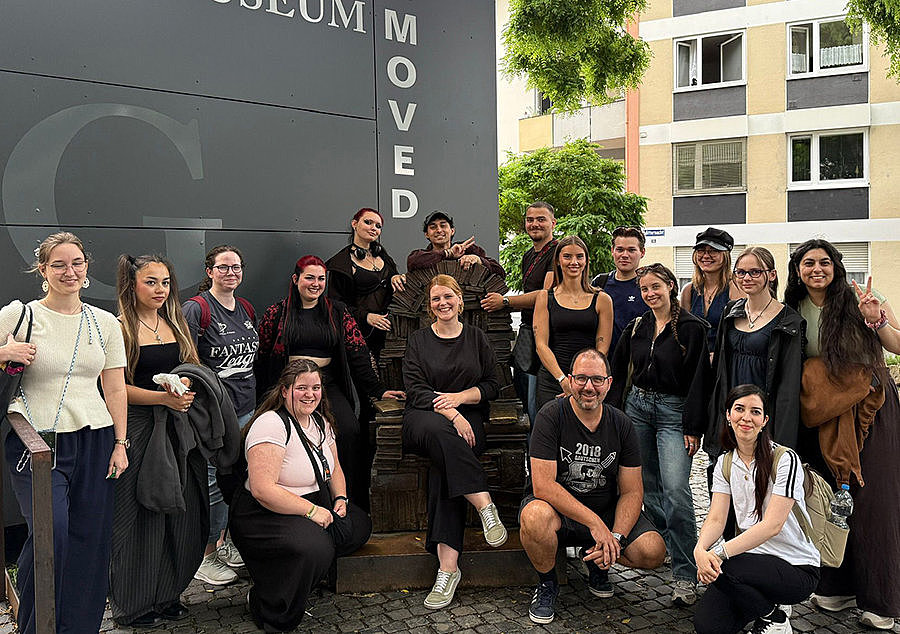 Gruppenfoto der Mediengestalter/-innen Digital und Print vor dem Gutenberg-Museum und der Bronzeskulptur „Büchersessel“ von Liesel Metten