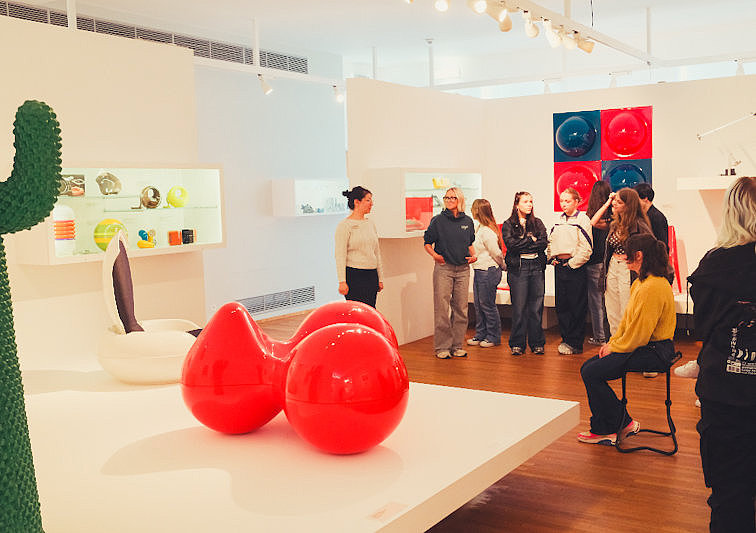 Moderne Designausstellung im Museum für Angewandte Kunst Köln mit farbigen Kunst- und Möbelobjekten. Im Vordergrund stehen zwei glänzend rote Skulpturen auf einem weißen Podest.