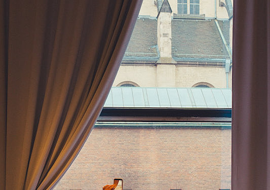 Besuchergruppe im Museum für Angewandte Kunst Köln blickt durch ein großes Fenster auf den Kölner Dom. Eine Person fotografiert die Aussicht mit einem Smartphone.