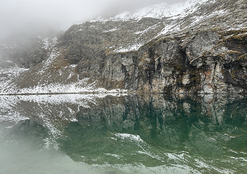Schneebedeckter Fels spiegelt sich in einem Bergsee