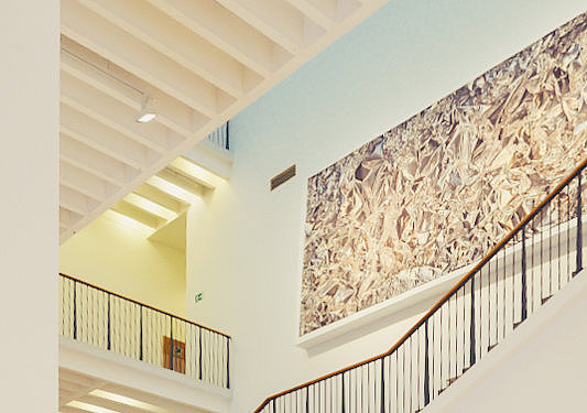 Blick in das hohe, offene Treppenhaus des Museum für Angewandte Kunst Köln mit mehreren Etagen und einer großformatigen Wandarbeit.